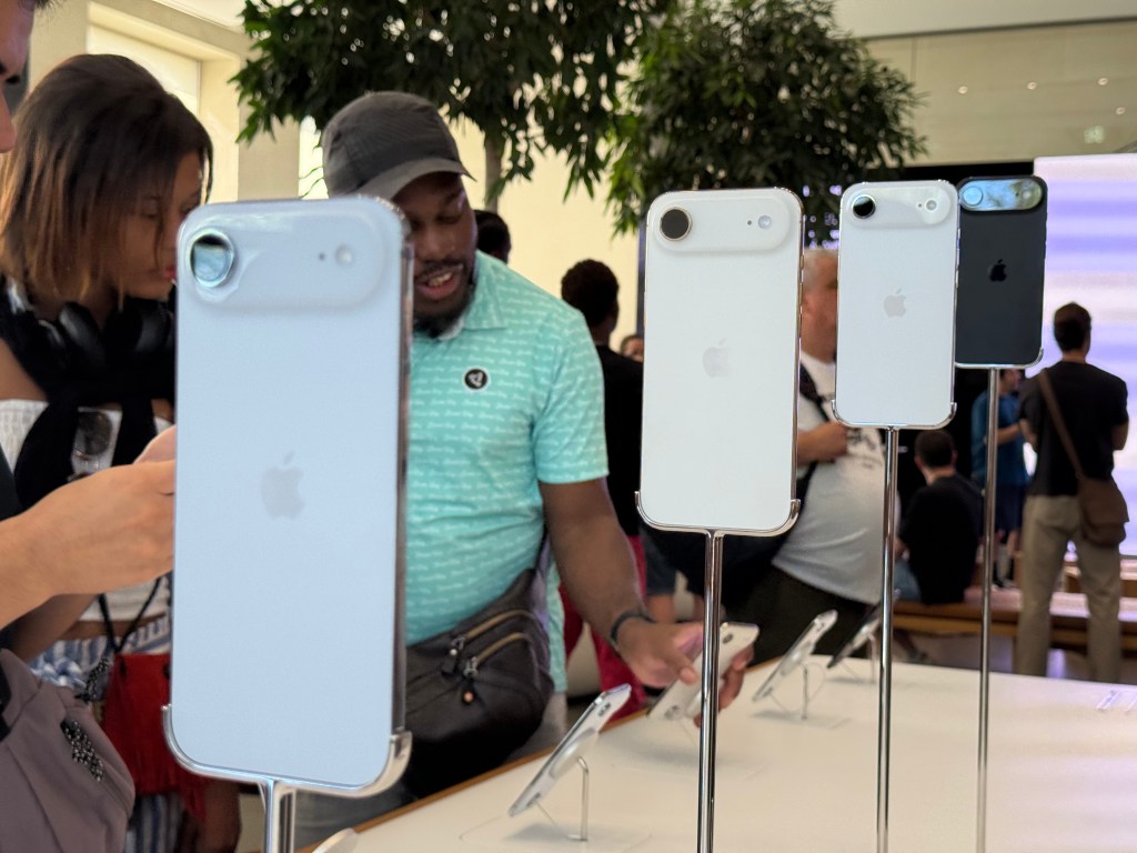 Diversos modelos de iPhone expuestos en un evento, con personas observando y probando los dispositivos.