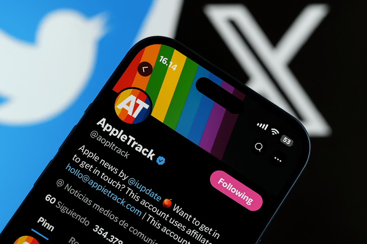 Close-up photo of the AppleTrack Twitter profile displayed on an iPhone screen, showing the AT logo, rainbow banner, and follower details, with the Twitter and X logos blurred in the background.
