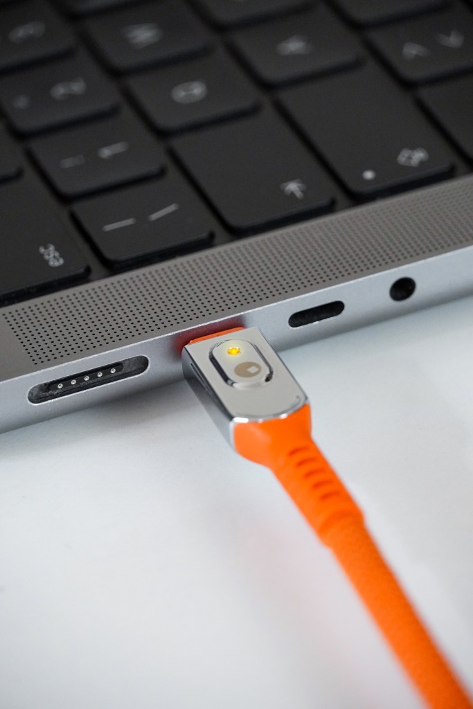 Close-up of a vibrant orange charging cable connected to a laptop, featuring a LED indicator.