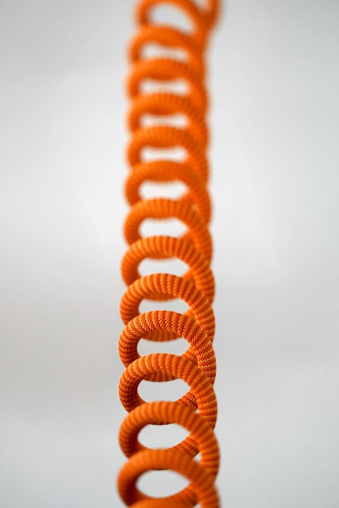 Cable enrollado de color naranja, diseñado para ser duradero y modular, con una apariencia textil sobre un fondo blanco.