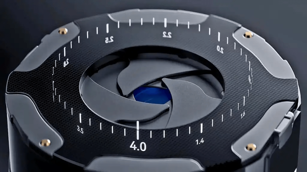 Primer plano de un mecanismo de apertura variable de cámara, con marcas numéricas visibles que indican la apertura. La estructura tiene un diseño moderno y sofisticado, mostrando un acabado en negro y detalles dorados.