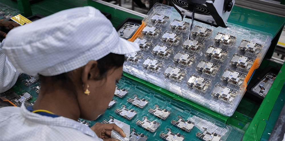 Trabajador en una línea de ensamblaje manipulando componentes electrónicos en una planta de producción de AirPods en India.