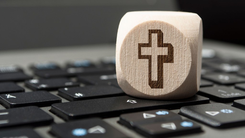 Un primer plano de un dado de madera con una cruz grabada sobre un teclado de computadora.