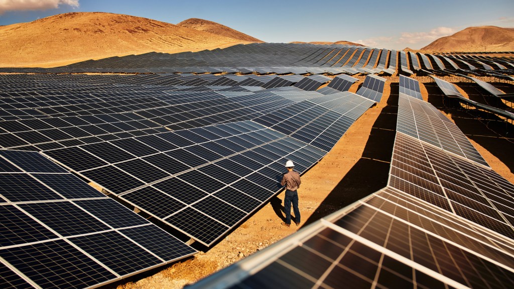 Un trabajador inspecciona un campo de paneles solares en un paisaje árido.