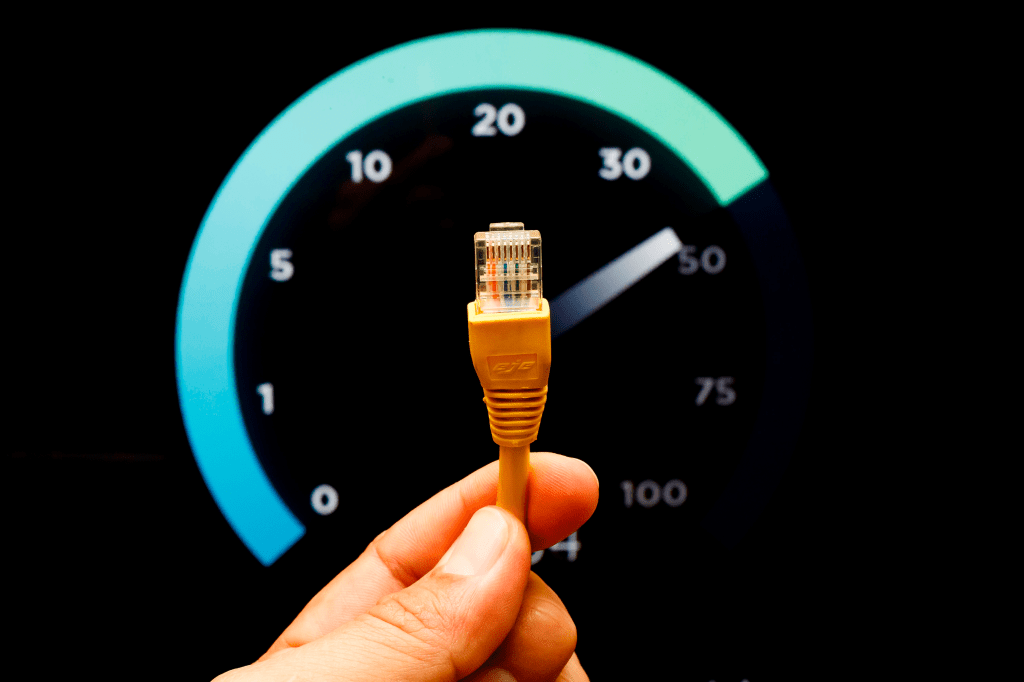 Un usuario sostiene un conector de cable de red mientras se muestra un medidor de velocidad de internet en el fondo.