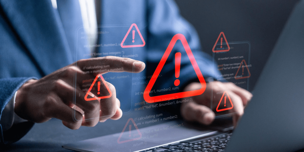 Un profesional en traje está interactuando con un ordenador portátil, frente a una pantalla que muestra múltiples señales de alerta en forma de triángulos rojos, simbolizando riesgos de ciberseguridad.