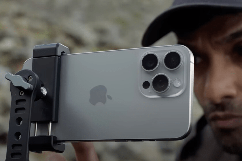 Un hombre sostiene un iPhone montado en un soporte de cámara, con un entorno natural difuminado al fondo.