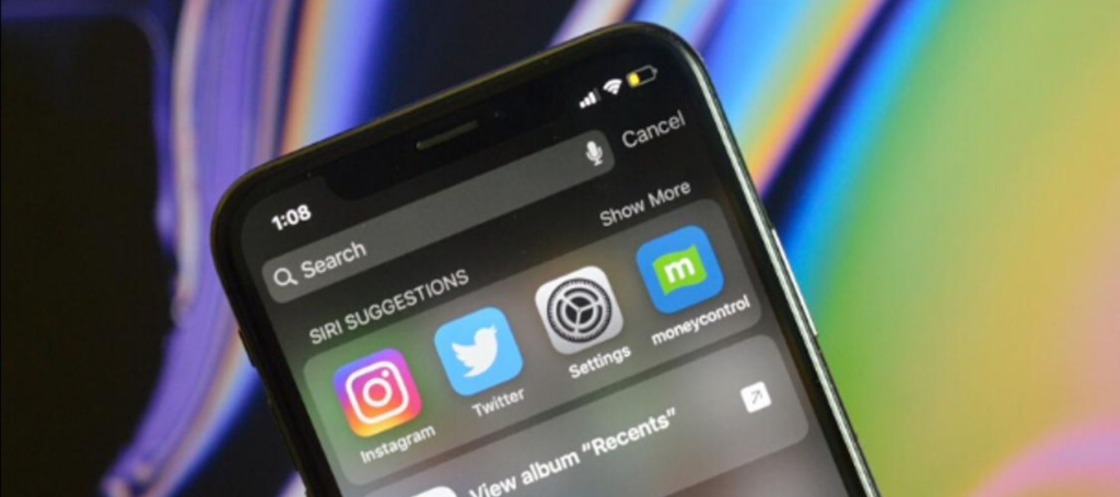 Imagen de un iPhone mostrando la interfaz de búsqueda con sugerencias de Siri, incluyendo íconos de aplicaciones como Instagram y Twitter, en un fondo colorido.