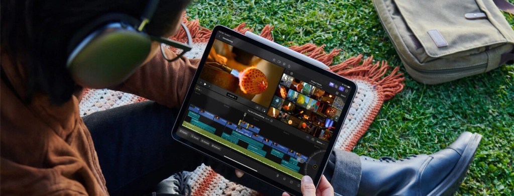 Una persona editando un video en una tablet mientras escucha con auriculares, sentada sobre un mat de picnic en un área verde.