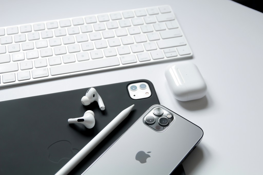 Un iPhone junto a unos AirPods, un Apple Pencil y un teclado, todos sobre una superficie blanca.