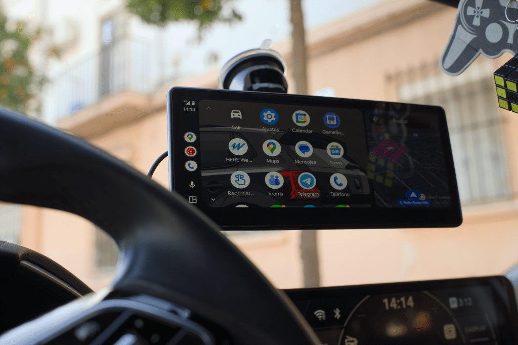 Pantalla de navegación montada en un coche, mostrando aplicaciones como mapas, mensajes y un fondo de ciudad.