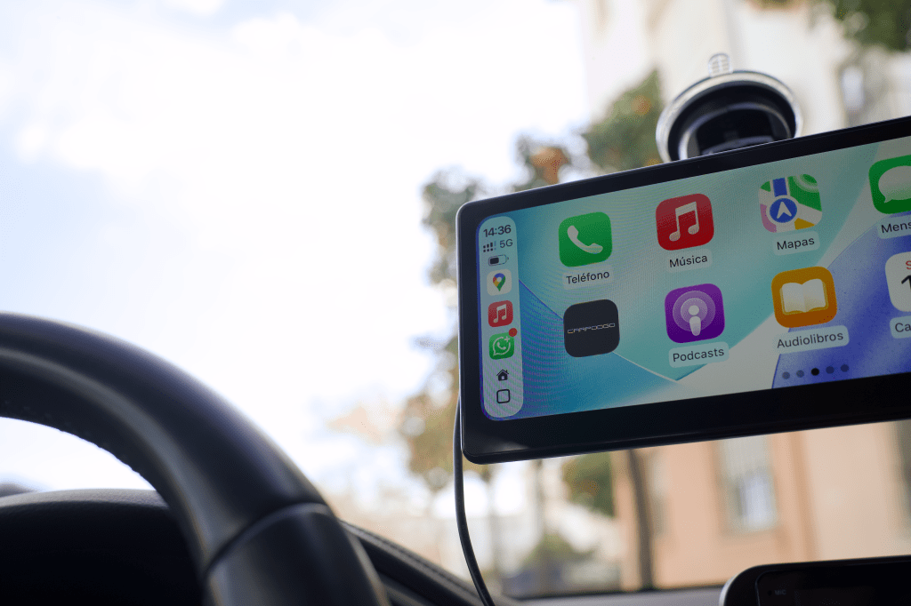 Pantalla de un smartphone mostrando aplicaciones como Teléfono, Música, Mapas, y Podcasts, vista desde el interior de un vehículo.