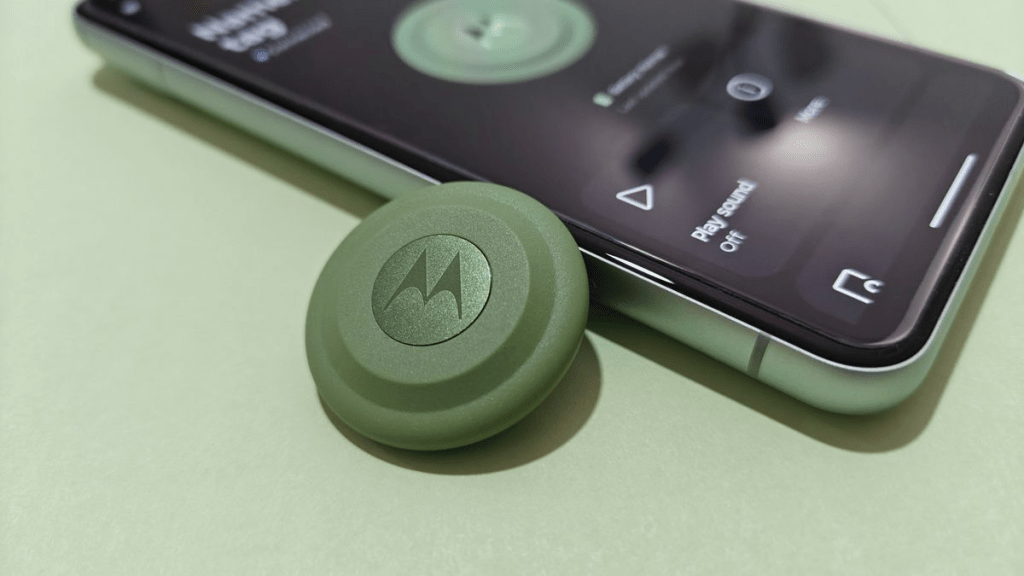 Un teléfono móvil junto a un dispositivo verde de la marca Motorola sobre un fondo verde claro.
