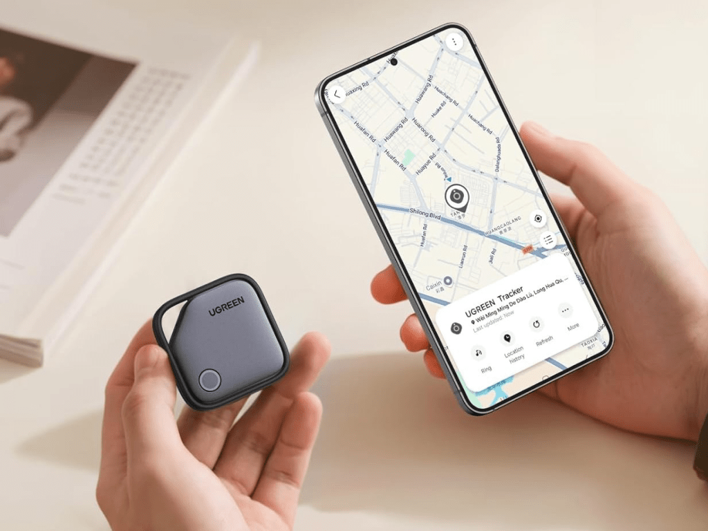 Una persona sostiene un rastreador UGREEN en una mano mientras que en la otra sostiene un smartphone mostrando un mapa con la ubicación del dispositivo.