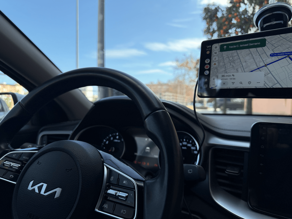 Interior de un coche Kia, mostrando el volante y una pantalla montada que indica direcciones de navegación.