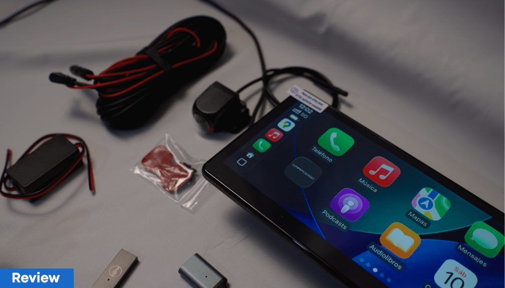 Pantalla de un dispositivo multimedia con iconos de aplicaciones como teléfono, música, podcasts, mapas, audiolibros y mensajes, acompañada de cables y accesorios.